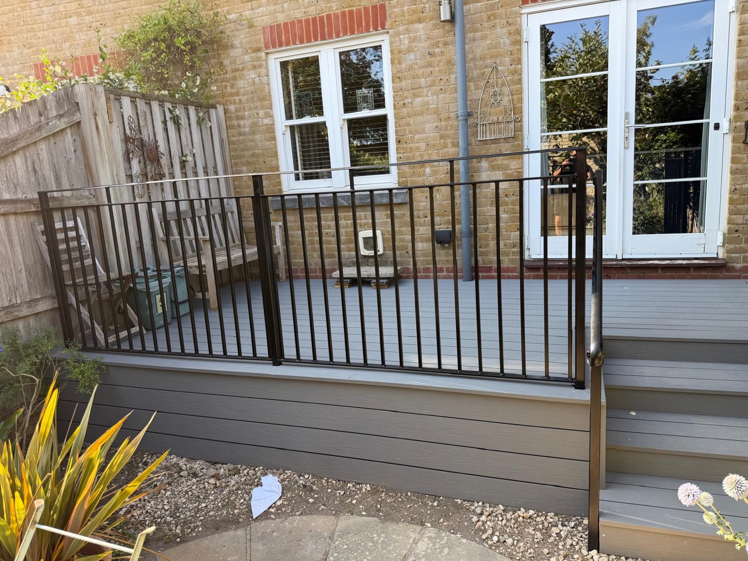 Raised grey decking beside the house with black vertical railings and matching edge boards